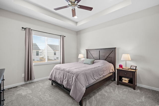 carpeted bedroom featuring baseboards, a raised ceiling, and a ceiling fan