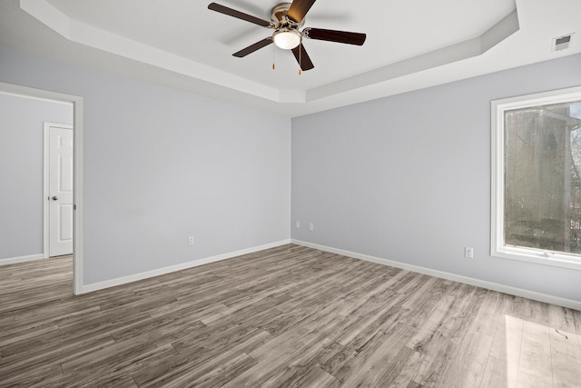 unfurnished room with visible vents, baseboards, a tray ceiling, and wood finished floors