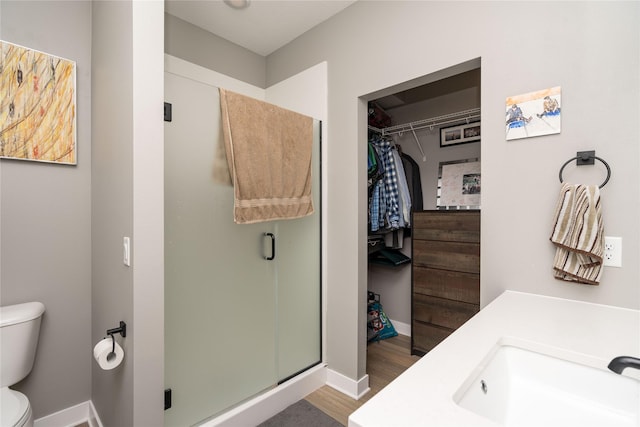 bathroom featuring toilet, wood finished floors, a shower stall, baseboards, and vanity