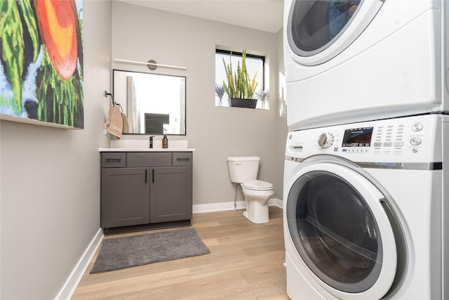 clothes washing area featuring stacked washer / dryer, light wood-style flooring, laundry area, and baseboards