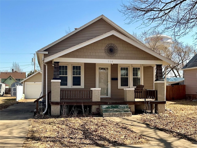 bungalow-style house with a porch, concrete driveway, an outbuilding, and a detached garage