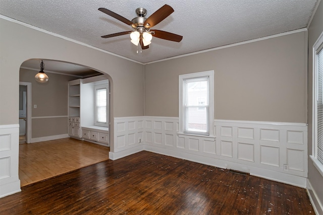 spare room featuring arched walkways, plenty of natural light, and hardwood / wood-style floors