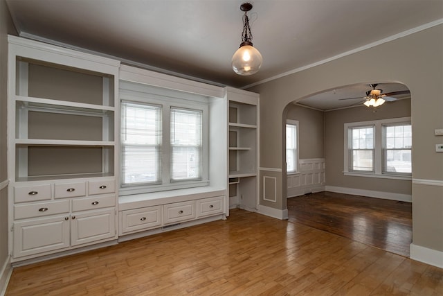 interior space featuring a ceiling fan, baseboards, light wood finished floors, arched walkways, and crown molding