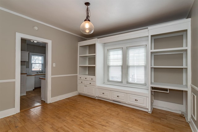 unfurnished dining area with visible vents, baseboards, ornamental molding, light wood-style floors, and a sink