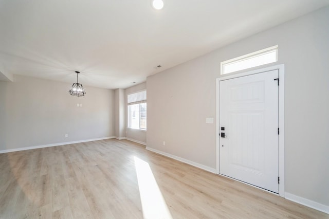 entryway with baseboards, an inviting chandelier, and light wood-style flooring