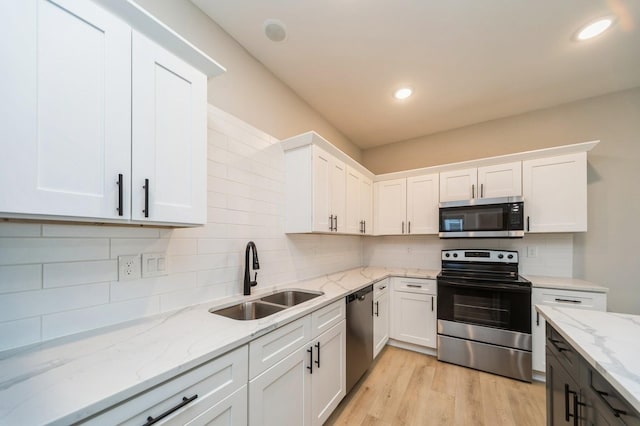 kitchen featuring tasteful backsplash, light wood-type flooring, appliances with stainless steel finishes, white cabinetry, and a sink