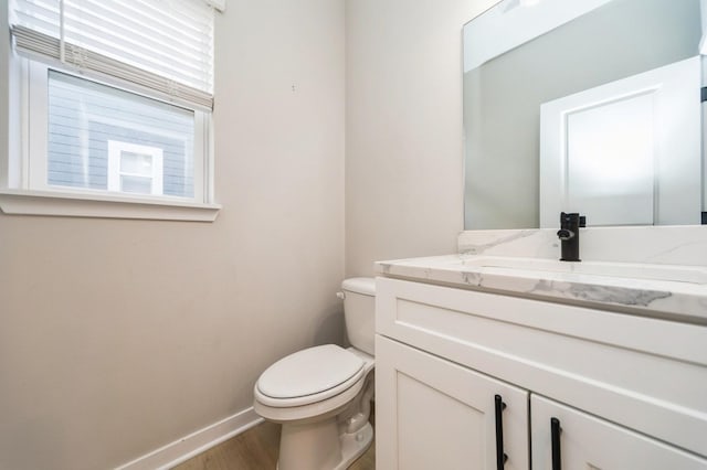 half bath featuring vanity, toilet, wood finished floors, and baseboards