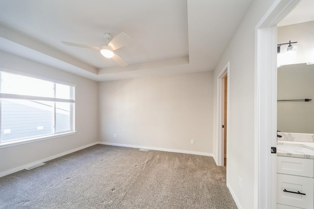 spare room with visible vents, baseboards, light colored carpet, a tray ceiling, and a ceiling fan