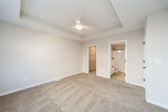 unfurnished bedroom featuring baseboards, a tray ceiling, a spacious closet, a closet, and light carpet