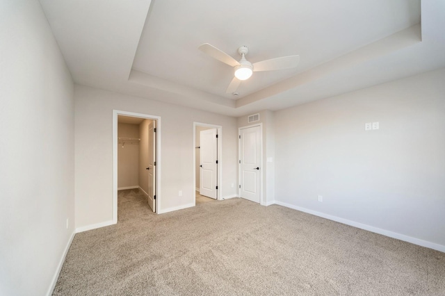 unfurnished bedroom with light carpet, a spacious closet, baseboards, and a tray ceiling