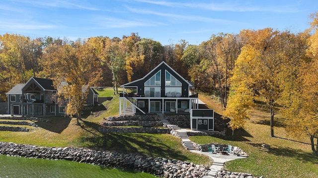 rear view of property featuring a water view, a patio, a yard, a sunroom, and stairs