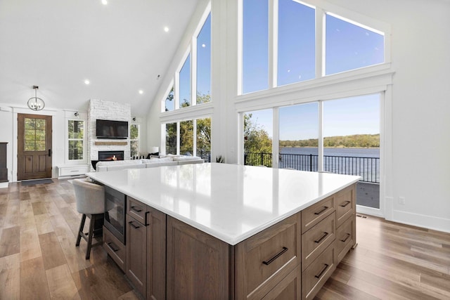 kitchen featuring high vaulted ceiling, light wood-style flooring, built in microwave, a stone fireplace, and a center island