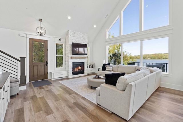 living area with stairway, high vaulted ceiling, a fireplace, a notable chandelier, and light wood-type flooring