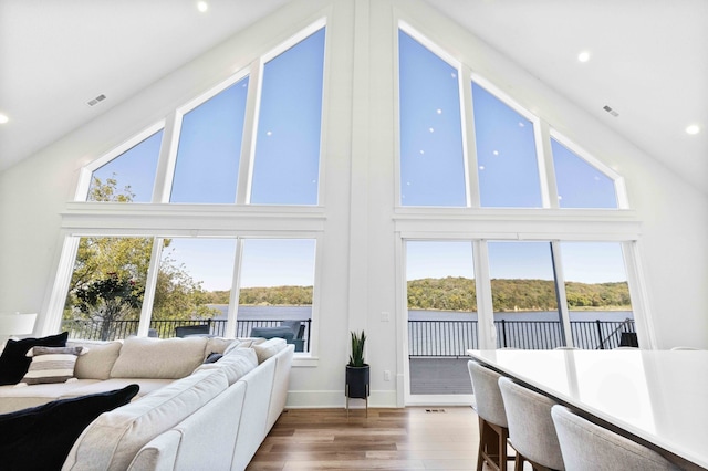 living area featuring a wealth of natural light, high vaulted ceiling, wood finished floors, and a water view