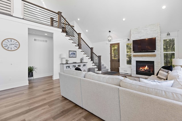 living area featuring visible vents, light wood-type flooring, stairs, and high vaulted ceiling