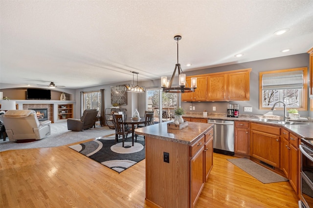 kitchen with a kitchen island, a fireplace, a sink, light wood-style floors, and dishwasher