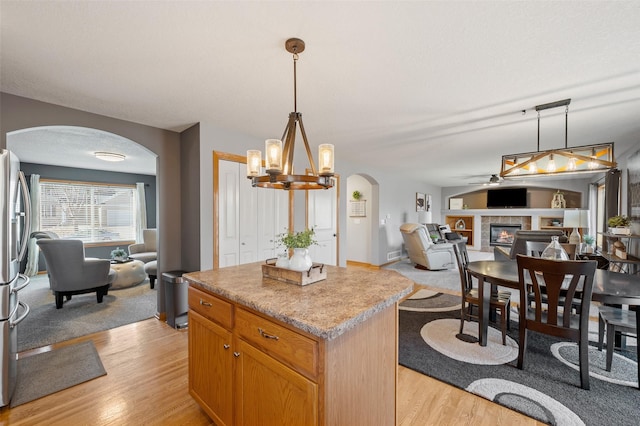 kitchen with light wood-style flooring, a kitchen island, open floor plan, arched walkways, and a fireplace