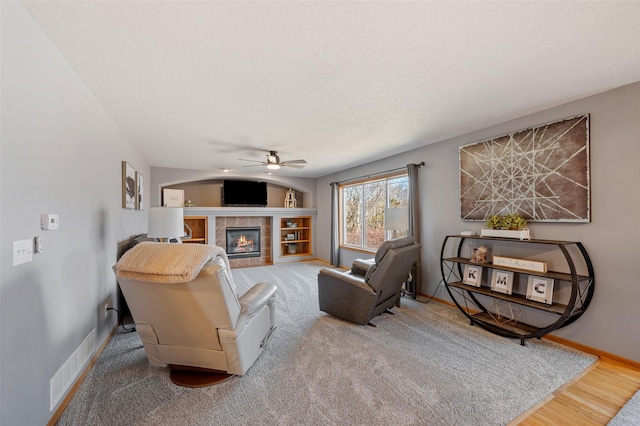 living area featuring visible vents, a tiled fireplace, a textured ceiling, baseboards, and ceiling fan