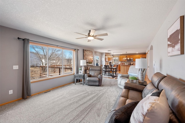 living area featuring visible vents, baseboards, light carpet, ceiling fan with notable chandelier, and arched walkways