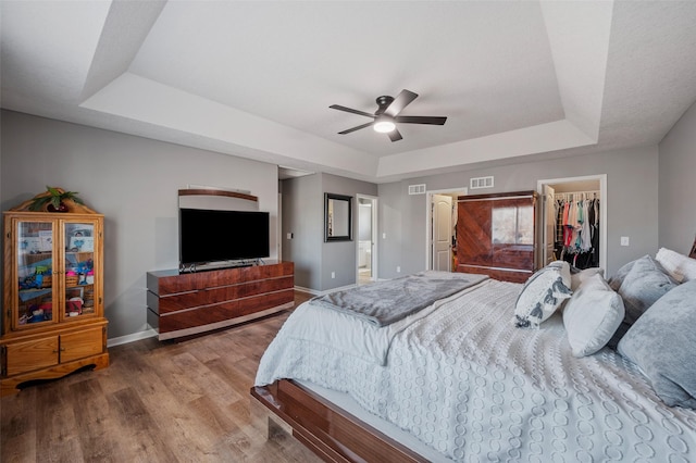 bedroom featuring visible vents, a walk in closet, wood finished floors, baseboards, and a raised ceiling