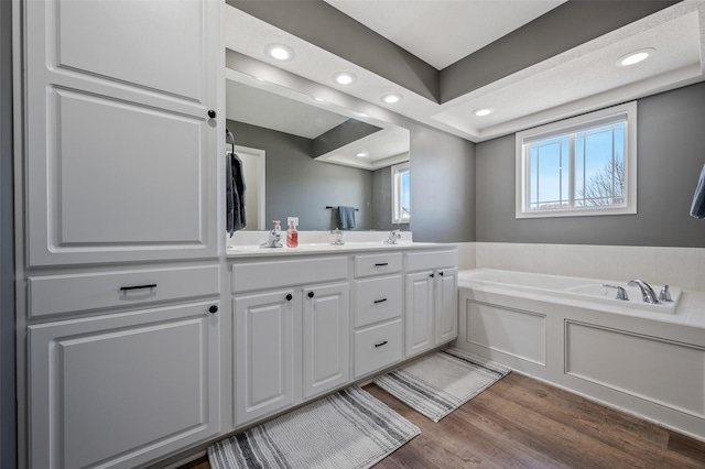 full bathroom featuring a sink, wood finished floors, recessed lighting, double vanity, and a bath