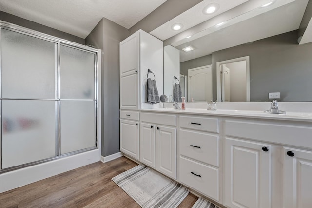 bathroom with double vanity, recessed lighting, a stall shower, wood finished floors, and a sink