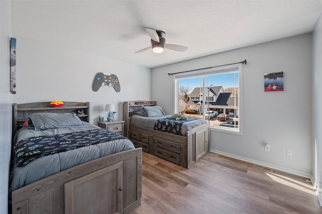 bedroom featuring baseboards, light wood-style floors, ceiling fan, and a textured ceiling