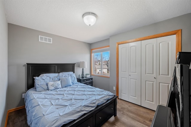 bedroom featuring a closet, visible vents, a textured ceiling, and wood finished floors