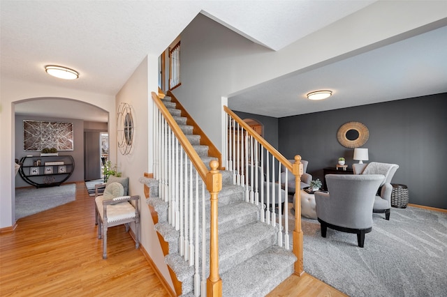 stairway featuring wood finished floors, baseboards, and arched walkways