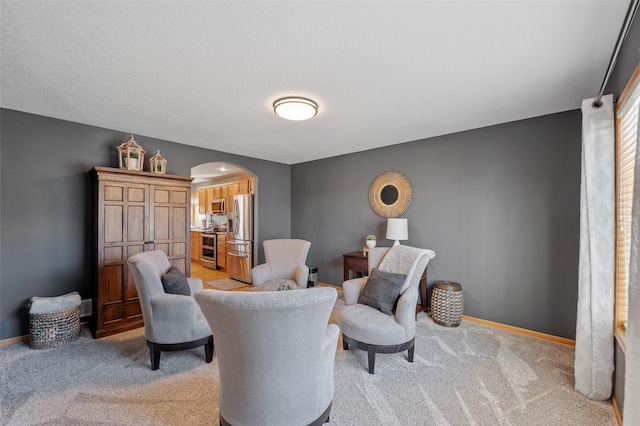 living area with light colored carpet, arched walkways, and baseboards