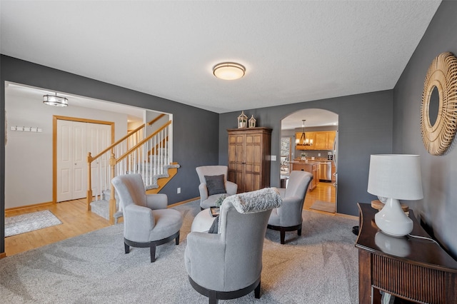 living room with baseboards, stairway, light colored carpet, light wood-style flooring, and arched walkways