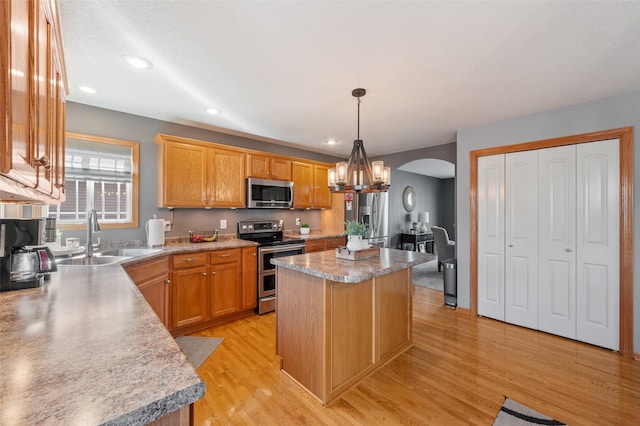 kitchen featuring light wood-type flooring, a sink, a center island, arched walkways, and appliances with stainless steel finishes