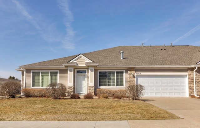 view of front of property with a front yard, driveway, an attached garage, a shingled roof, and stone siding