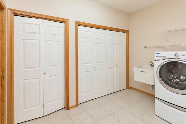 laundry room with baseboards, laundry area, light tile patterned flooring, washer / clothes dryer, and a sink