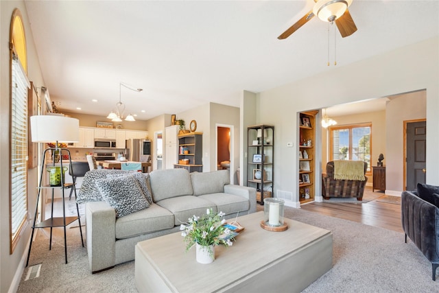 living area with light wood-type flooring, visible vents, ceiling fan with notable chandelier, recessed lighting, and baseboards