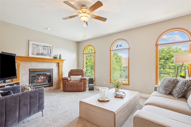 carpeted living room featuring baseboards, ceiling fan, and a tiled fireplace