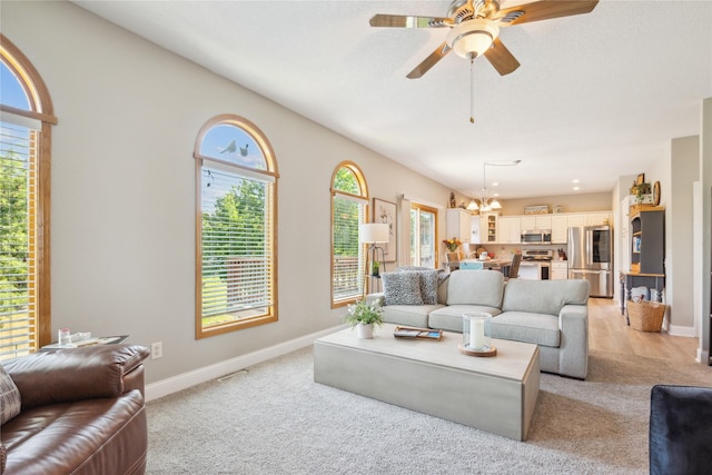 living area with ceiling fan with notable chandelier, a healthy amount of sunlight, and baseboards