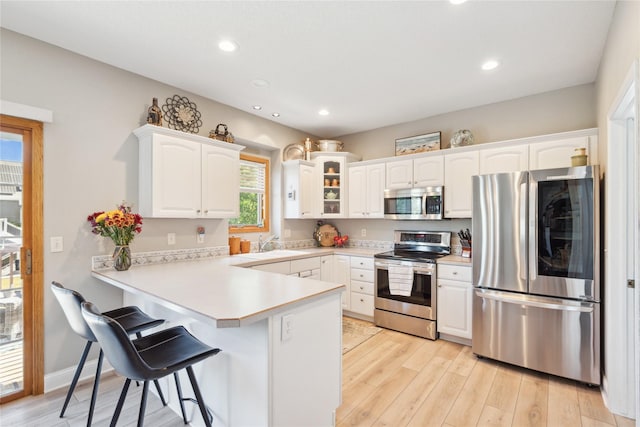 kitchen featuring a breakfast bar area, a peninsula, light wood-style flooring, appliances with stainless steel finishes, and white cabinetry