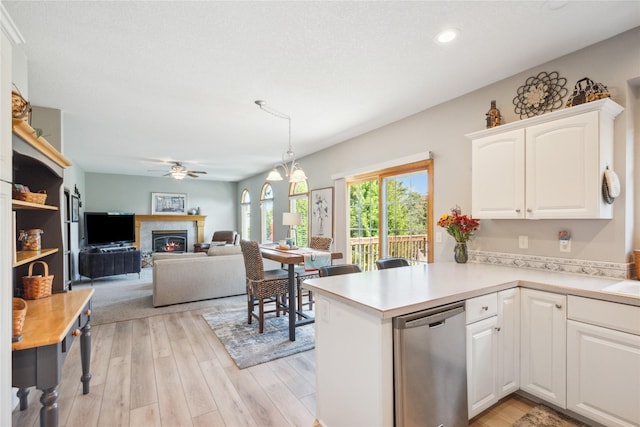 kitchen featuring a glass covered fireplace, white cabinetry, a peninsula, light countertops, and stainless steel dishwasher