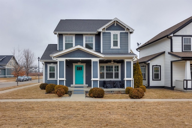 craftsman house featuring covered porch, a shingled roof, and a front yard