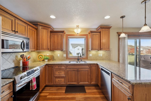 kitchen with brown cabinets, appliances with stainless steel finishes, a peninsula, dark wood-style floors, and a sink