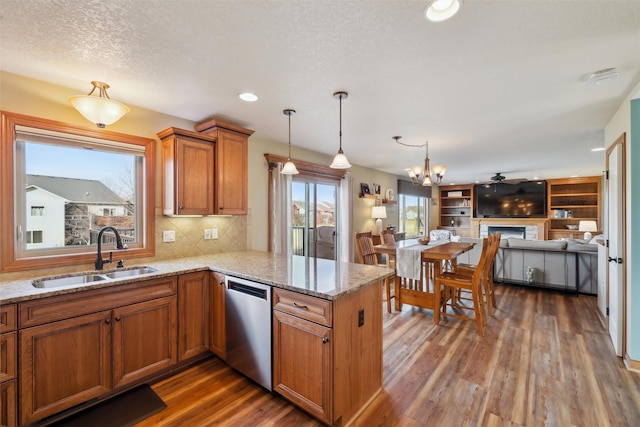 kitchen with a sink, stainless steel dishwasher, dark wood finished floors, a peninsula, and brown cabinetry