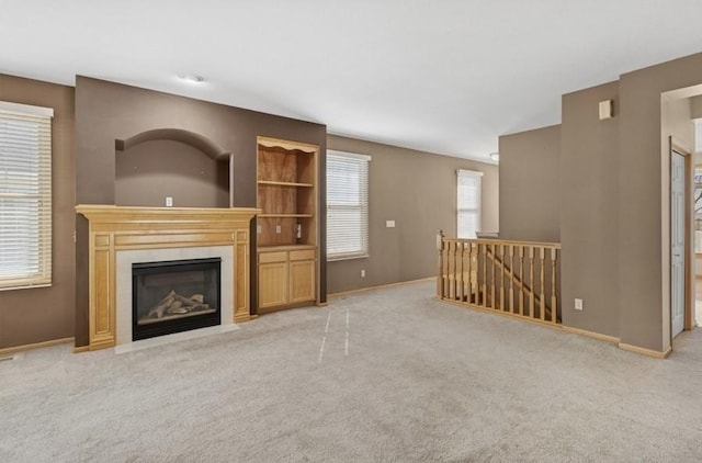 unfurnished living room featuring carpet, a fireplace with flush hearth, a healthy amount of sunlight, and baseboards