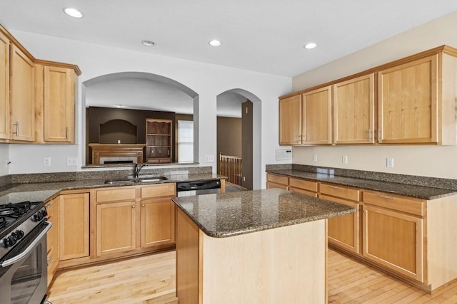 kitchen featuring stainless steel gas range oven, light wood-type flooring, black dishwasher, dark stone countertops, and a sink