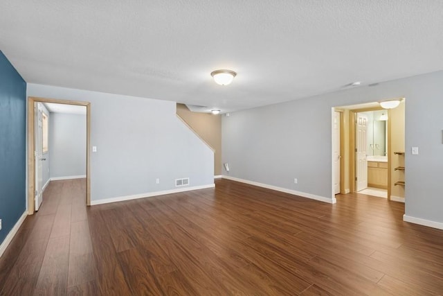 spare room featuring dark wood finished floors, visible vents, a textured ceiling, and baseboards