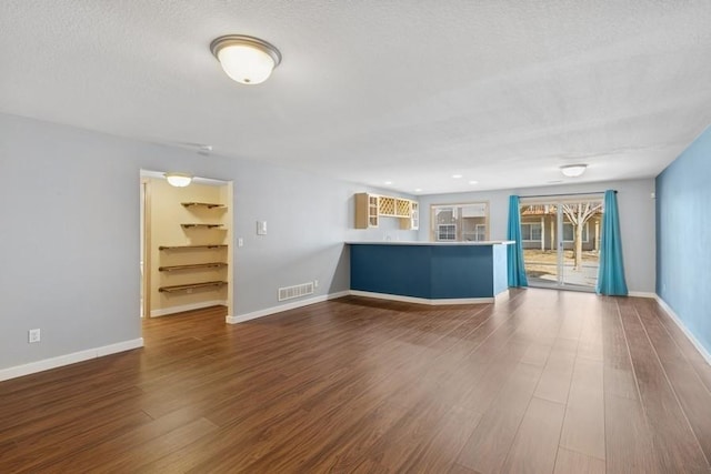 unfurnished living room featuring baseboards, wood finished floors, visible vents, and a textured ceiling