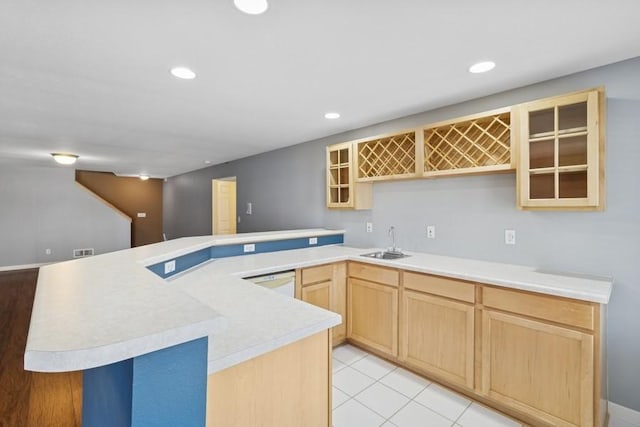 kitchen with light brown cabinets, a sink, a peninsula, light countertops, and glass insert cabinets