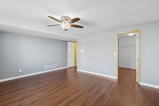 spare room featuring visible vents, baseboards, ceiling fan, and dark wood-style flooring