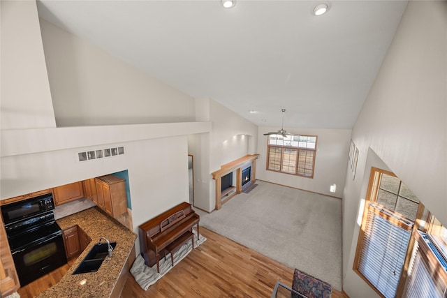 living room with visible vents, a fireplace with flush hearth, light wood-style flooring, recessed lighting, and lofted ceiling