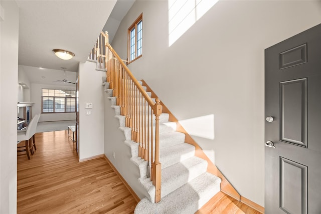 stairs with baseboards, wood finished floors, and a ceiling fan